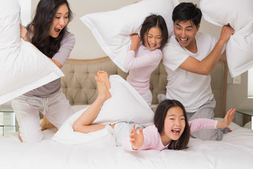 Cheerful kids and parents having pillow fight on bed at home &#8211; pt