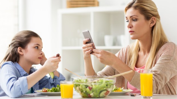 Mãe e filha na mesa com seus telefones