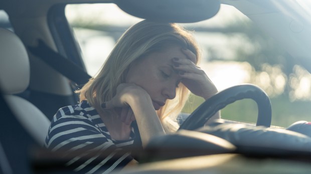 Mulher ao volante com expressão de tristeza e depressão, parecendo rezar com desânimo
