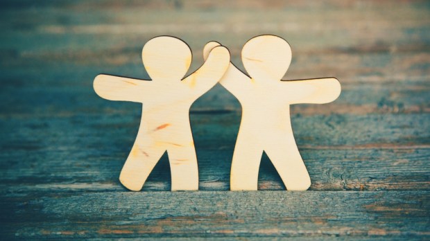 Wooden little men holding hands on wooden boards background