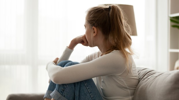 Vista lateral de una joven mirando a la ventana sentada en el sofá en casa. Frustrada mujer confusa se siente infeliz problema en la vida personal